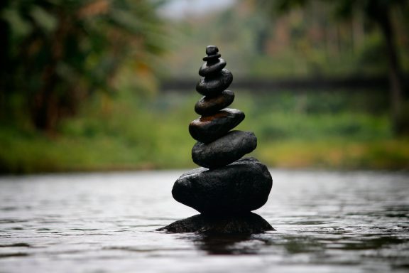 Balanced Health & Sleep Stacked stones balanced on a tranquil body of water, surrounded by greenery.